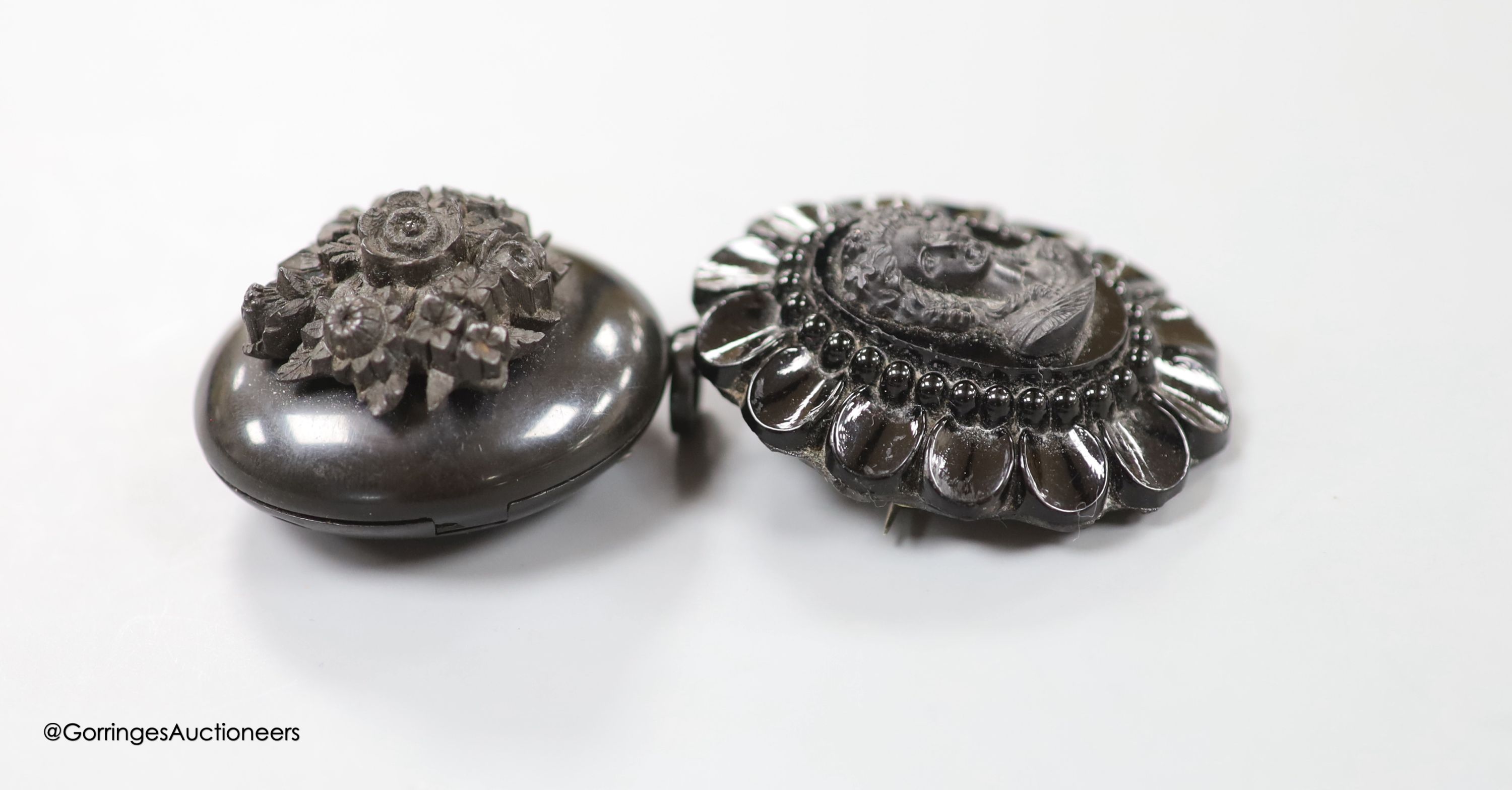 A jet oval pendant, carved with a bunch of flowers, 41mm and a similar brooch, carved with the bust of a lady.